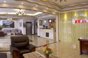 Een hotellobby met een receptiebalie, zithoek en een kroonluchter.