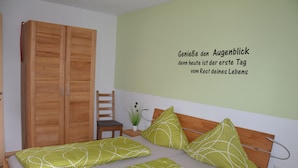 Un dormitorio con una cama, un armario de madera, una mesita con una planta y una pared con una cita motivacional.