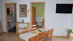 Un comedor con una mesa, sillas, un televisor y un florero con flores.