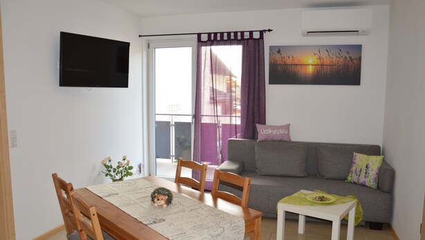 Una sala de estar con televisor, sofá y una mesa de comedor con sillas.