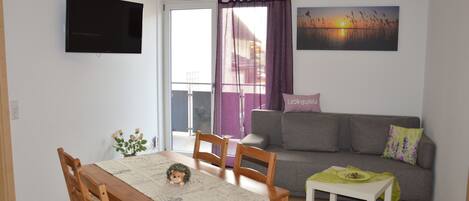 A living room with a TV, sofa, and a dining table with chairs.