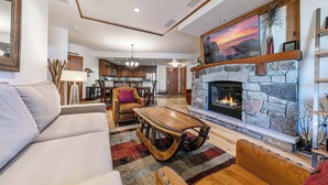 A spacious living room with a stone fireplace, a large painting, and a cozy seating area. - Big Horn Lodge 307 - Slopeside in Village (Truckee)