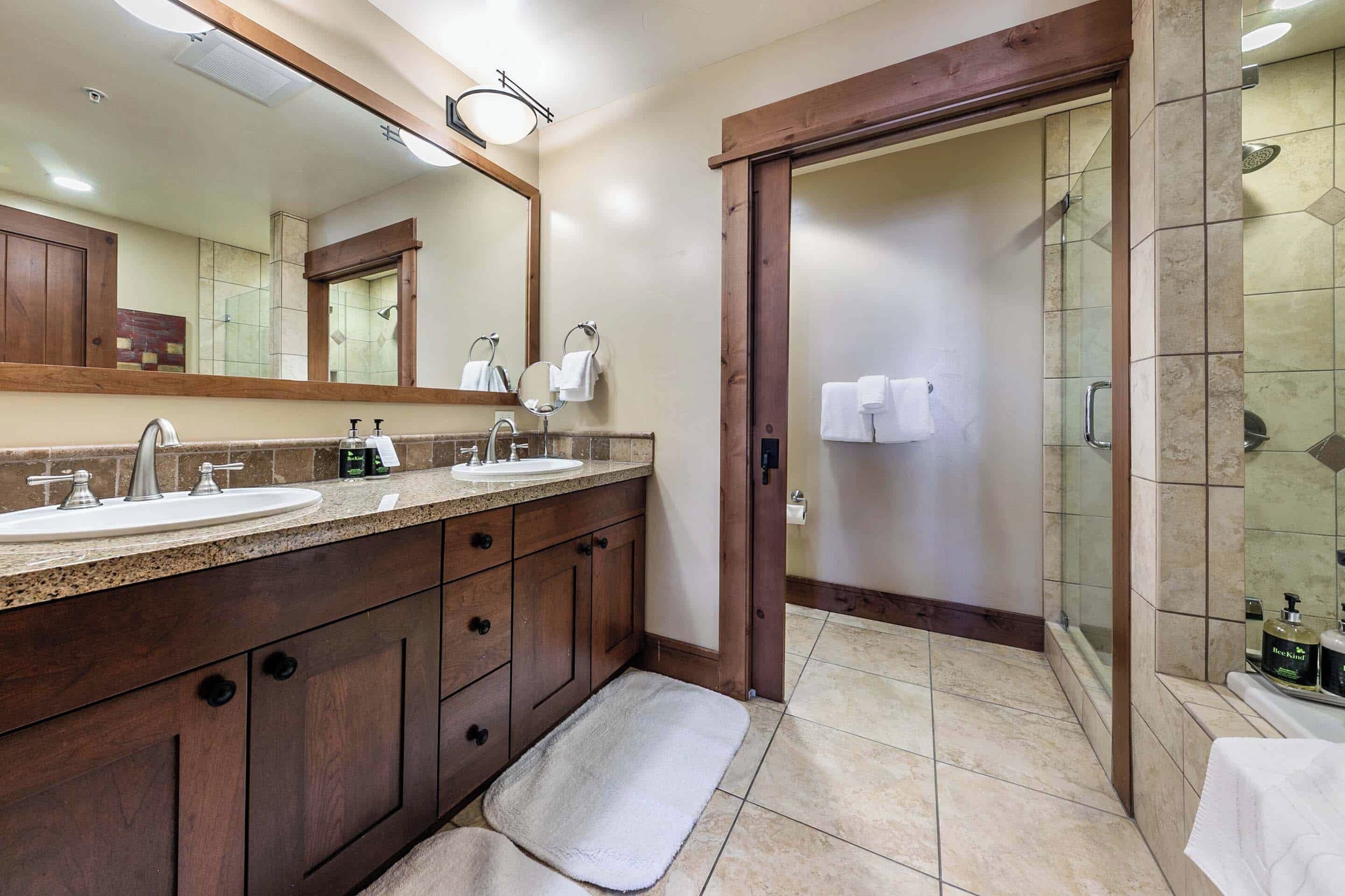 A modern bathroom with two sinks, a large mirror, and a walk-in shower.