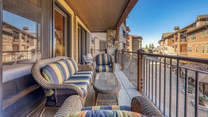 A balcony with wicker furniture, a stone accent wall, and a view of neighboring buildings. - Big Horn Lodge 307 - Slopeside in Village (Truckee)