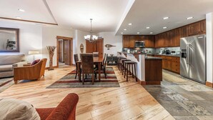 A spacious kitchen with wooden cabinets, a stainless steel refrigerator, and a dining area with a wooden table and chairs. - Big Horn Lodge 307 - Slopeside in Village (Truckee)