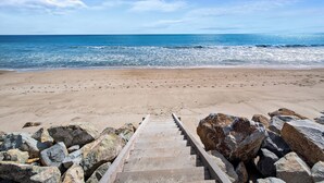 Une plage avec un escalier en bois menant à la rive, entourée de gros rochers.