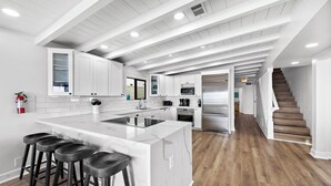 Une cuisine moderne avec des meubles blancs, un grand îlot central doté de tabourets de bar et un escalier en bois menant à un autre niveau.
