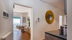 Une chambre d’hôtel moderne avec un plancher en bois, un coin repas comprenant une table et des chaises, un grand miroir et une vue sur la mer par la fenêtre.