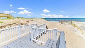 A wooden boardwalk leading to a beach with a wooden fence and a wooden bridge in the background. - Magnificent oceanfront home in South Nags Head! (South Nags Head)