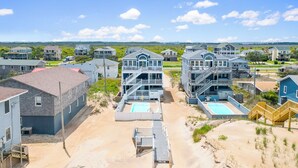 A coastal residential area with multiple two-story houses featuring balconies, swimming pools, and sandy beaches. - Magnificent oceanfront home in South Nags Head! (South Nags Head)