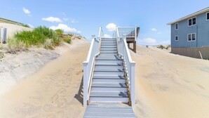 A staircase leading to a beach house with a wooden deck and a sandy path. - Magnificent oceanfront home in South Nags Head! (South Nags Head)