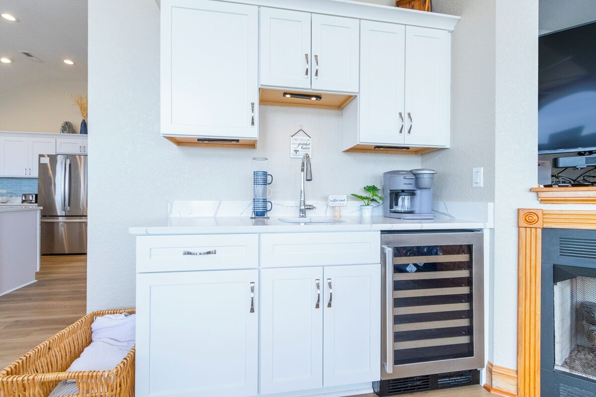 A modern kitchen with white cabinetry, a built-in dishwasher, a coffee station, and a fireplace.