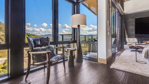 A spacious living area with large windows offering a view of the outdoors, a comfortable seating area with a sofa and chairs, a small round table, and a floor lamp. - One Snowmass West 601 (Snowmass)