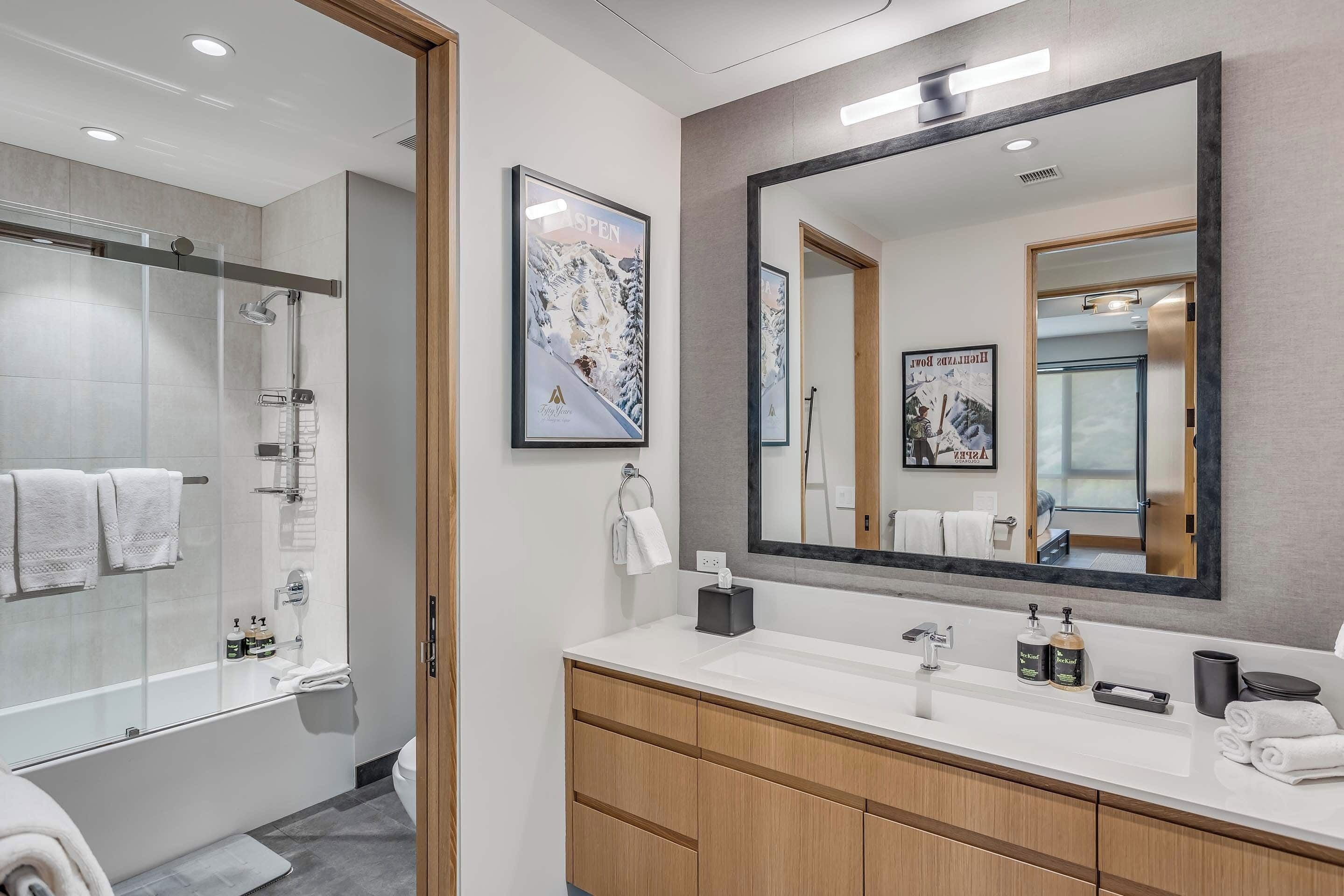 A modern bathroom with a glass-enclosed shower, a large mirror, and a wooden vanity.