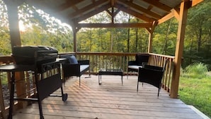 A covered outdoor deck with a grill, two chairs, and a table. - Inspiration Station (Pikeville)