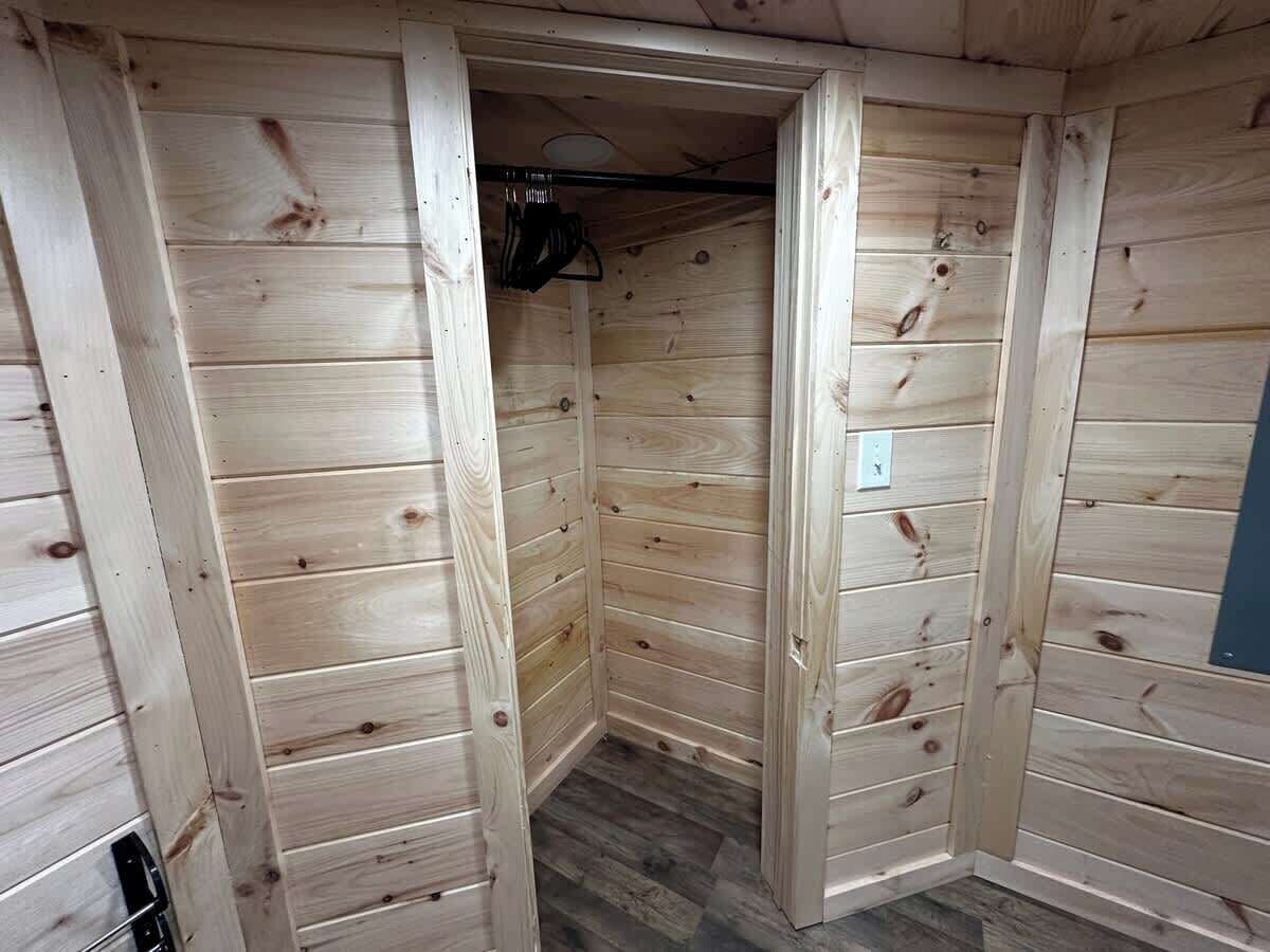 Habitación de madera con una puerta que da a un armario, un enchufe y una lámpara en el techo.