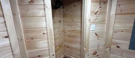 Habitación de madera con una puerta que da a un armario, un enchufe y una lámpara en el techo.