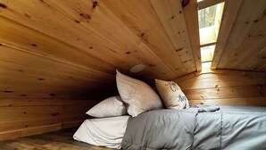 A wooden cabin interior with a bed, pillows, and a skylight. - Inspiration Station (Pikeville)