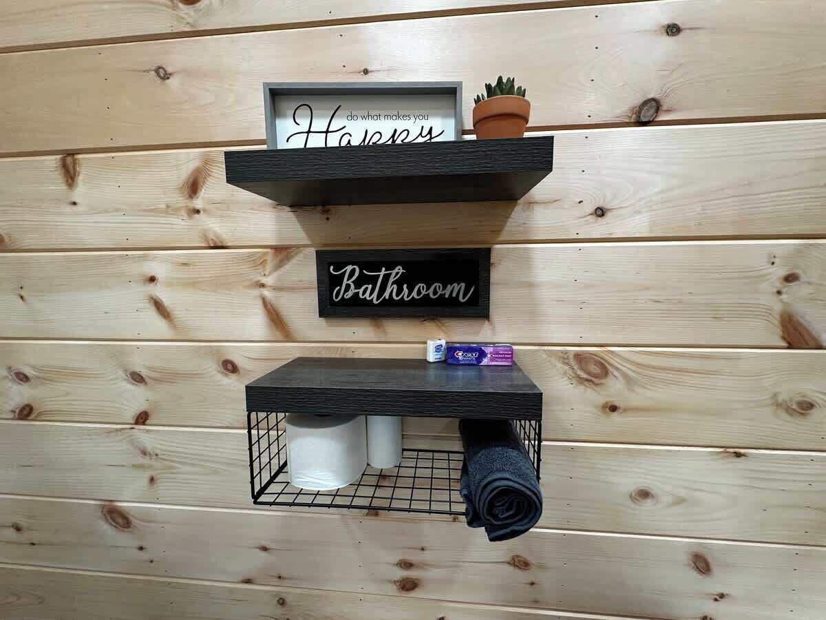Un bany amb una prestatgeria que conté un cartell emmarcat, una planta en test i una tovallola estovada.