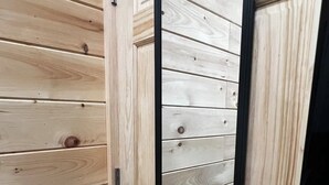 A wooden door with a black frame, a visible handle, and a reflection of a wooden wall. - Inspiration Station (Pikeville)