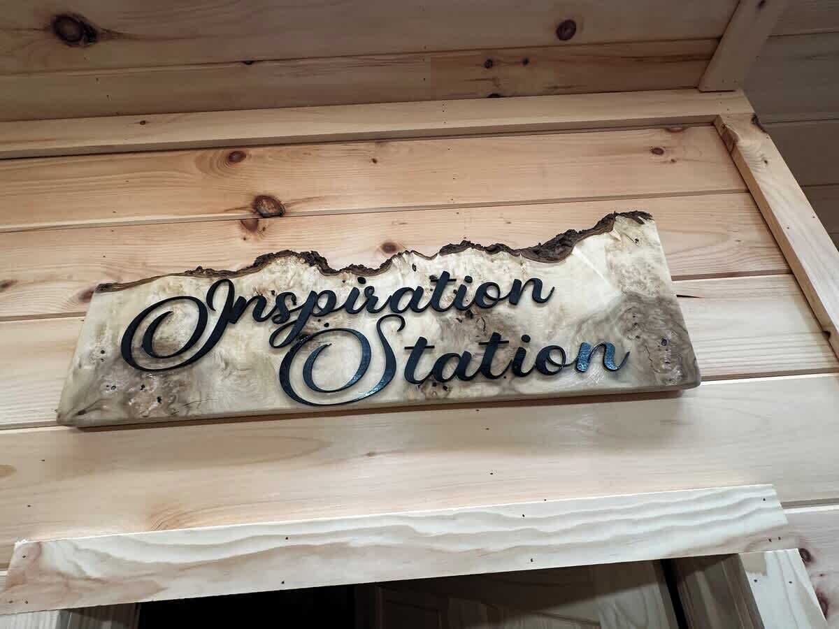 Ein Holzschild mit dem Schriftzug 'Inspiration Station' an einer Holzwand.