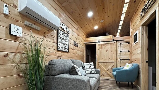 A wooden interior with a sofa, a blue armchair, and a potted plant. - Inspiration Station (Pikeville)