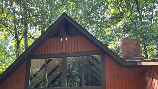 A wooden cabin with a large window, a wooden deck, and a staircase leading to the entrance. - Cozy Winston-Salem Vacation Cabin (Winston-Salem)