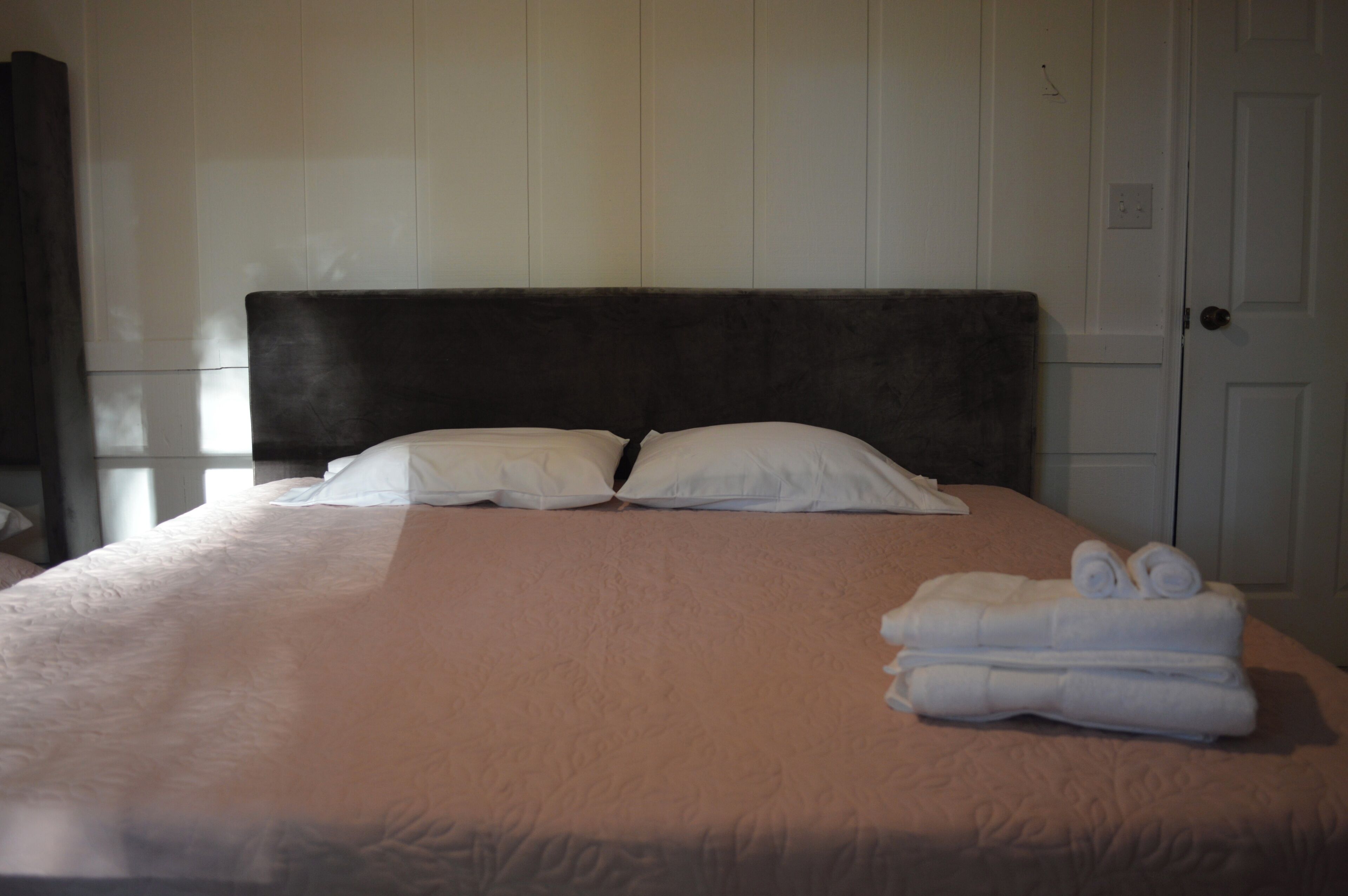 A neatly made bed with white linens and a dark headboard, accompanied by a pair of folded towels on the bed.