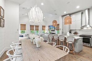 A modern kitchen with white cabinetry, a wooden dining table, wicker chairs, and pendant lighting. - Close to Seaside ~ Fully Stocked Kitchen ~ Golf Cart ~ Two Community Pools (Santa Rosa Beach)