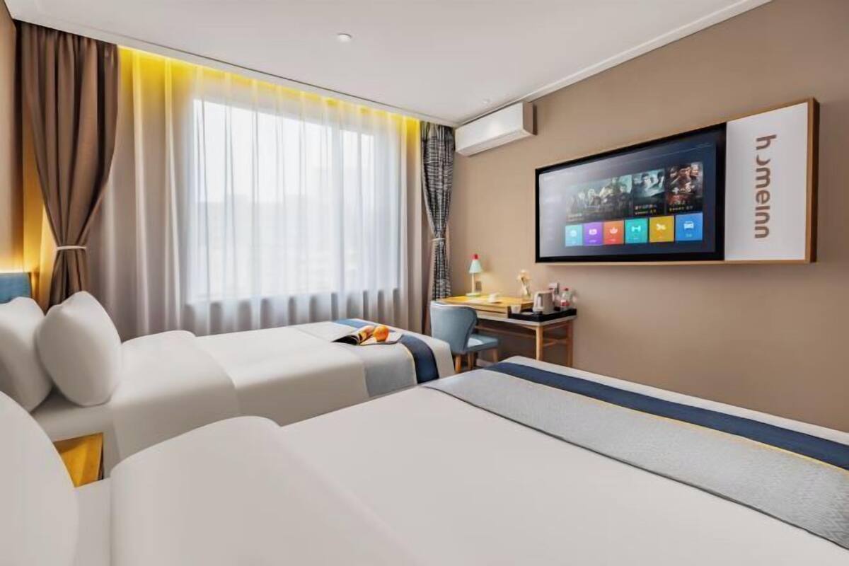 A hotel room with two beds, a desk, a chair, a TV, and a window with curtains.