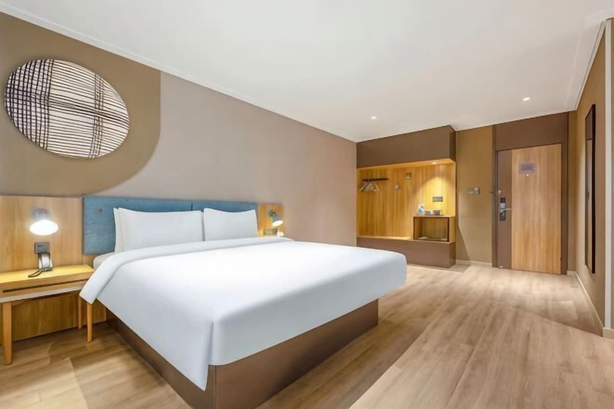 Ett modernt hotellrum med en stor säng, sängbord med lampor, en garderob i trä och en rund väggdekoration.
