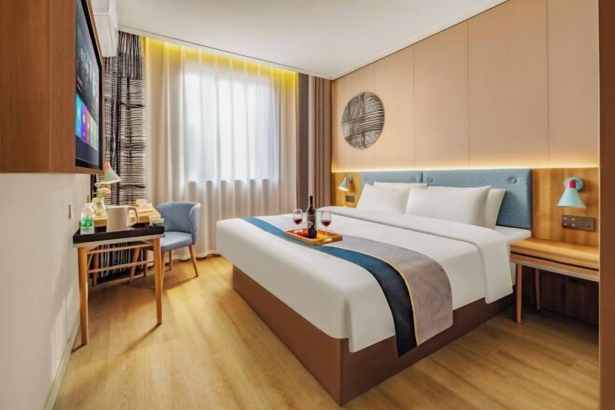 A hotel room with a bed, bedside tables, a desk with a chair, a TV, and a window with curtains.