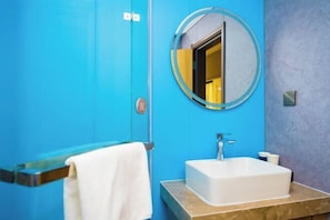 A bathroom with a blue wall, a white sink, a round mirror, and a towel hanging on a towel rack.