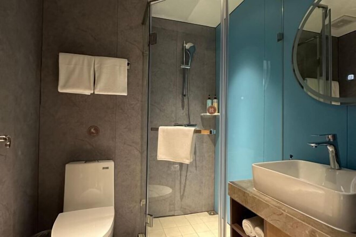 A modern bathroom with a glass shower enclosure, a white toilet, and a large sink with a mirror.