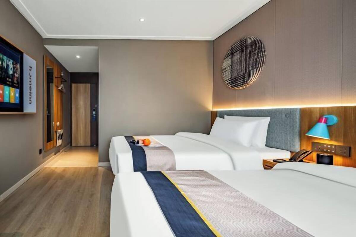 A hotel room with two beds, a TV, a wall-mounted lamp, and a wooden floor.