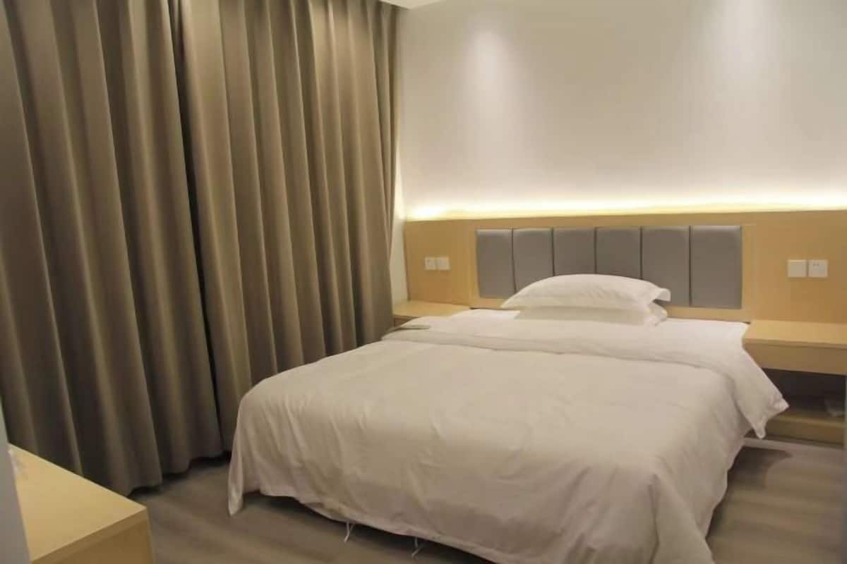 A hotel room with a bed, curtains, a bedside table, and a headboard.