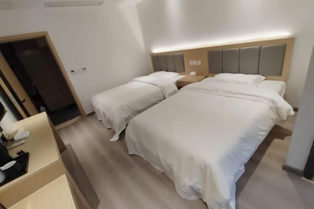 A hotel room with two beds, a bedside table, a desk, and a door.