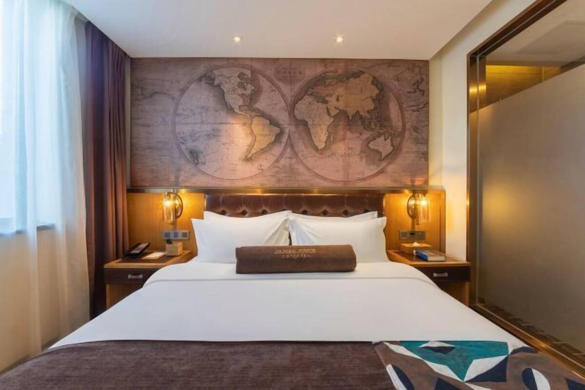 A hotel room with a large bed, a world map on the wall, and a brown headboard.