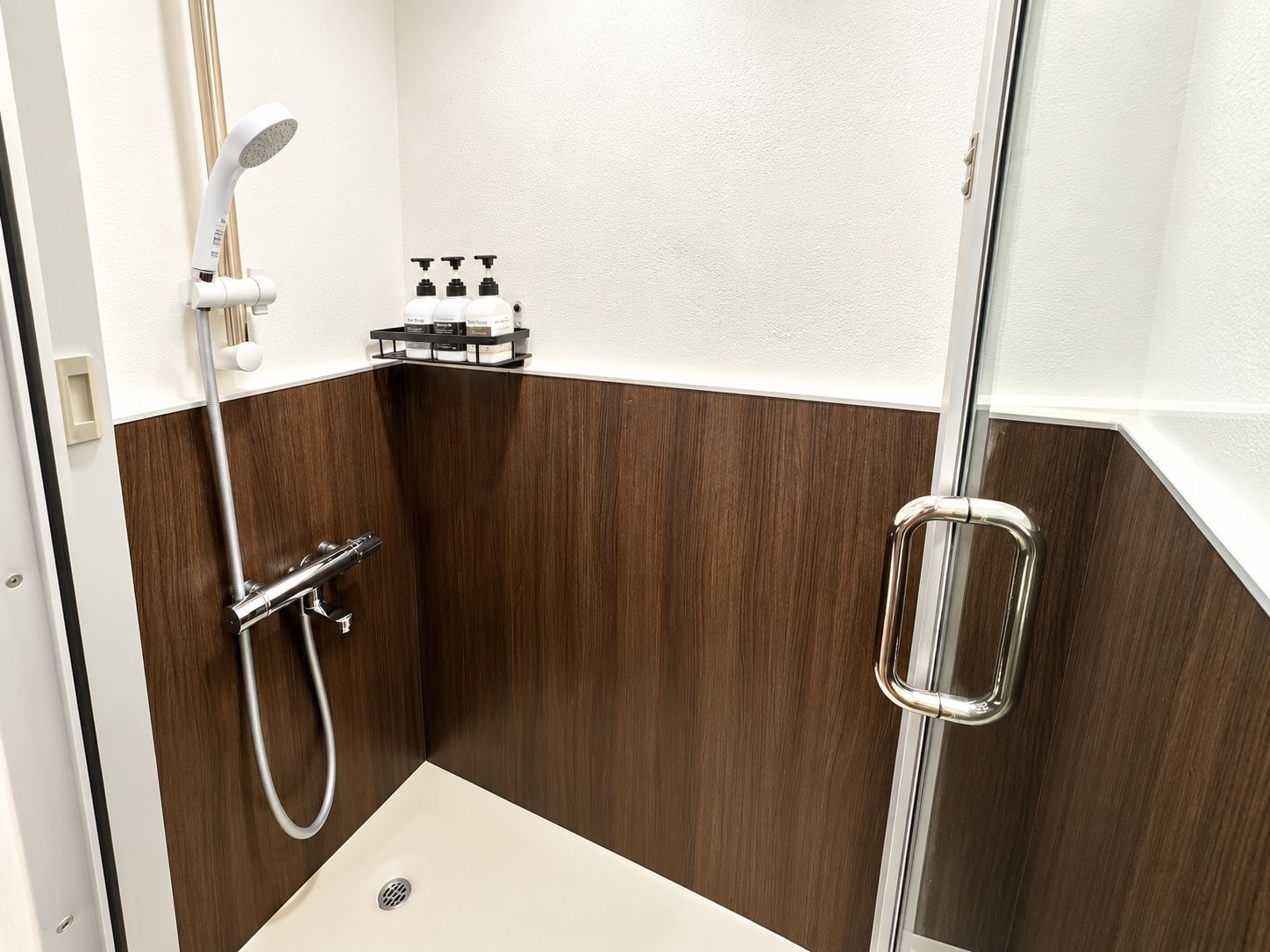 A small, modern shower area with a handheld showerhead, a glass shower enclosure, and a soap dispenser shelf.
