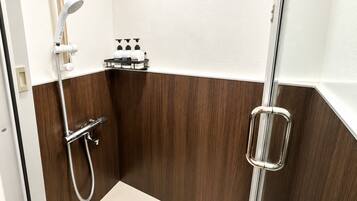 A small, modern shower area with a handheld showerhead, a glass shower enclosure, and a soap dispenser shelf.