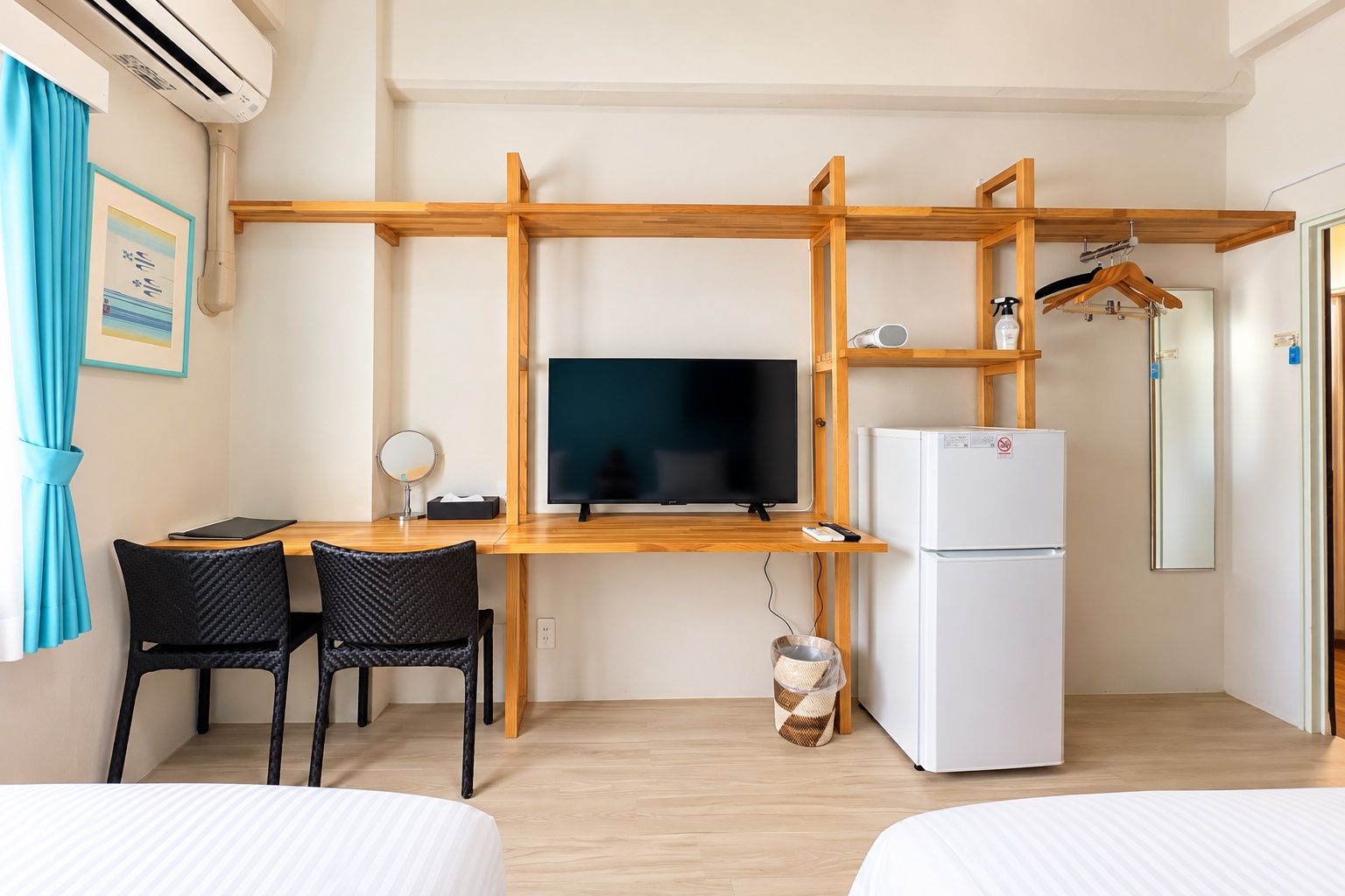 A hotel room with a wooden desk, a television, a refrigerator, two black chairs, and a bed.