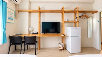 A hotel room with a wooden desk, a television, a refrigerator, two black chairs, and a bed.