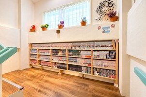 Una biblioteca infantil con estanterías de madera llenas de libros, una ventana con cortinas y un letrero con un número en la pared.