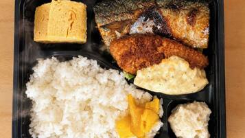 Una comida en un recipiente negro con arroz, un pescado, un elemento empanizado y salsa cremosa.