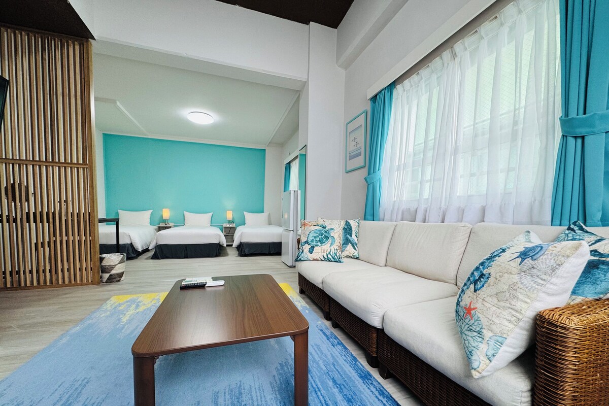 Een hotelkamer met twee bedden, een bank, een salontafel en een groot raam met gordijnen.