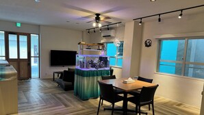 A dining area with a table and chairs, a fish tank, and a television in the background. - SimpleStayORIHIME (Ishigaki)