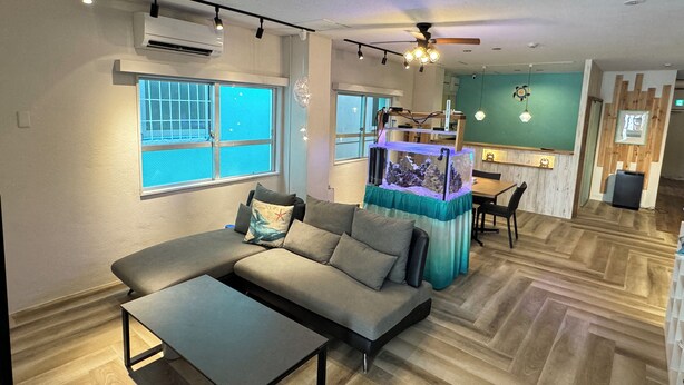 A modern living room with a sectional sofa, a coffee table, and a fish tank. - SimpleStayORIHIME (Ishigaki)