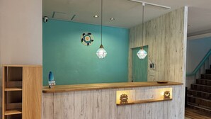 A reception desk with a wooden finish, a teal wall, and a hanging light fixture. - SimpleStayORIHIME (Ishigaki)