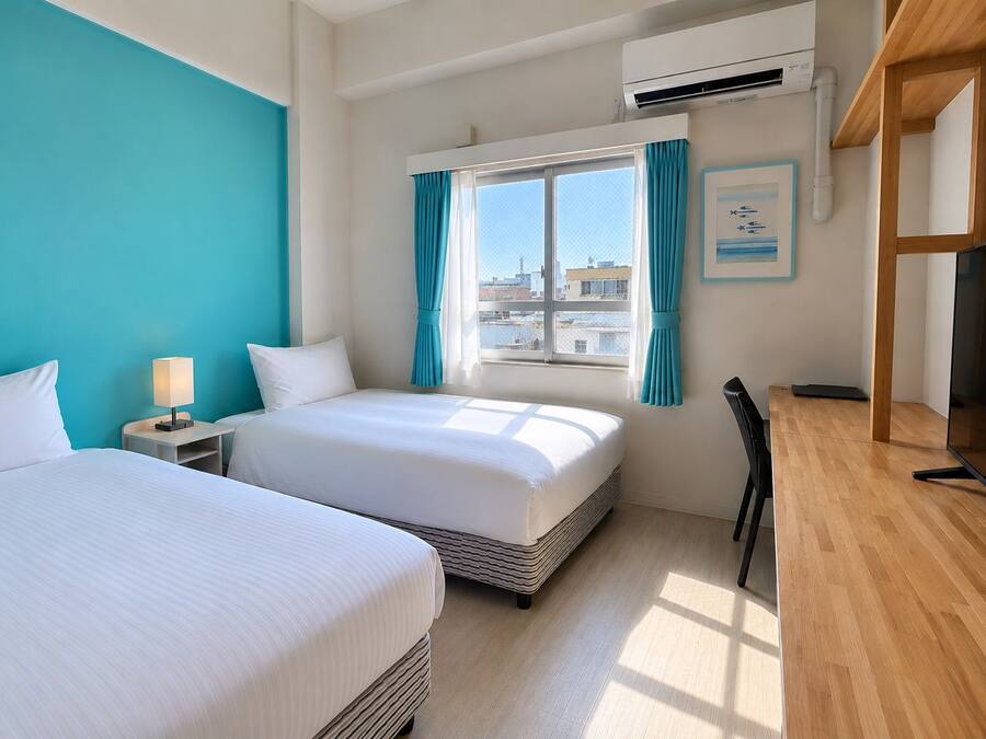 A hotel room with two beds, a desk, a chair, a TV, and a window with curtains.