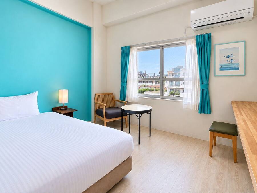 A hotel room with a bed, a desk, a chair, a small table, and a window with curtains.